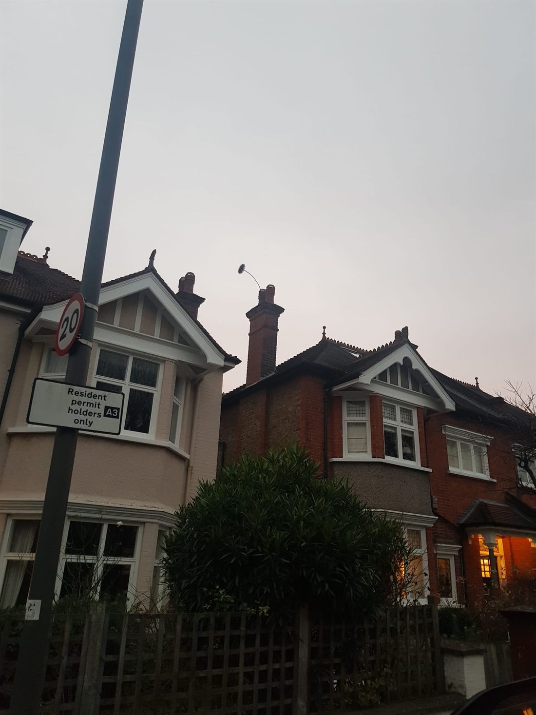 A sweep's brush showing above a chimney pot at dusk