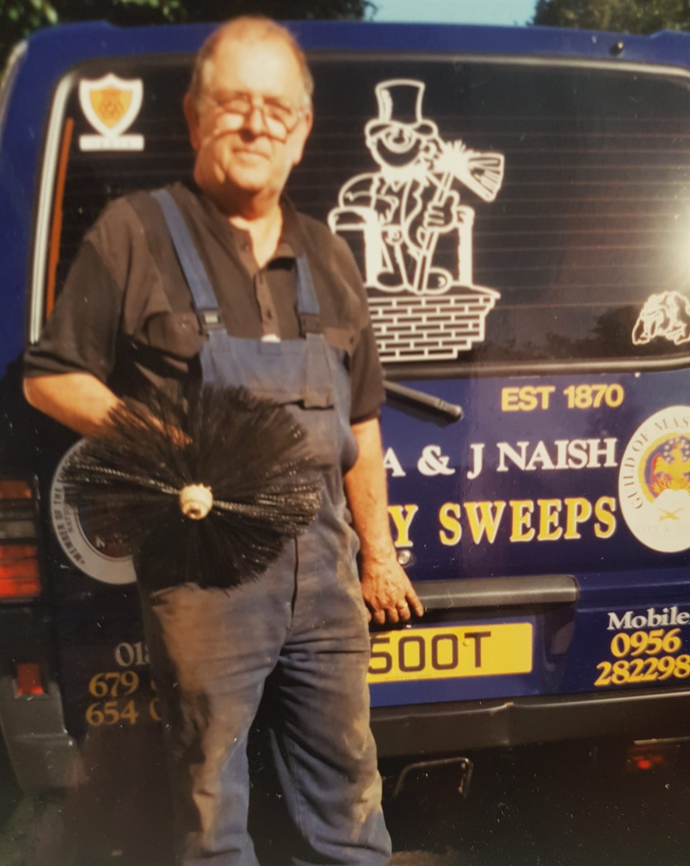 Alan's father standing with his chimney brush beside the old A & J Naish Chimney Sweeps van, marked EST 1870